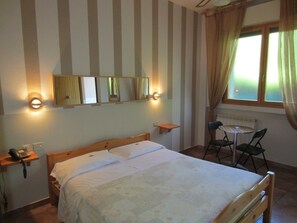 A bedroom with a bed, bedside tables, a desk with chairs, and a window with curtains. - Hotel Montemorello (Sesto Fiorentino)