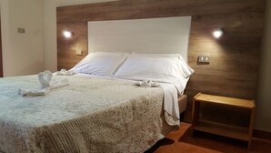 Un lit bien fait, avec du linge de lit blanc et une serviette, une tête de lit en bois et un éclairage de chevet.