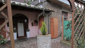 Une cour avec un sol en pierre, un jardinière centrale abritant un petit arbre et une pergola en bois.