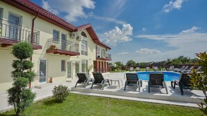 A two-story house with a swimming pool, outdoor seating, and a well-maintained lawn.