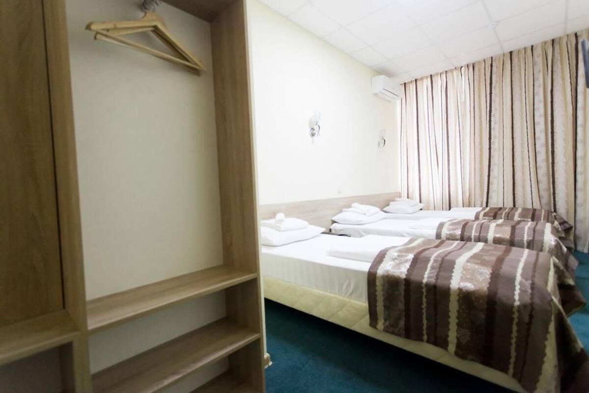 Hotellihuone, jossa on kaksi sänkyä, puinen vaatekaappi ja vaateteline.