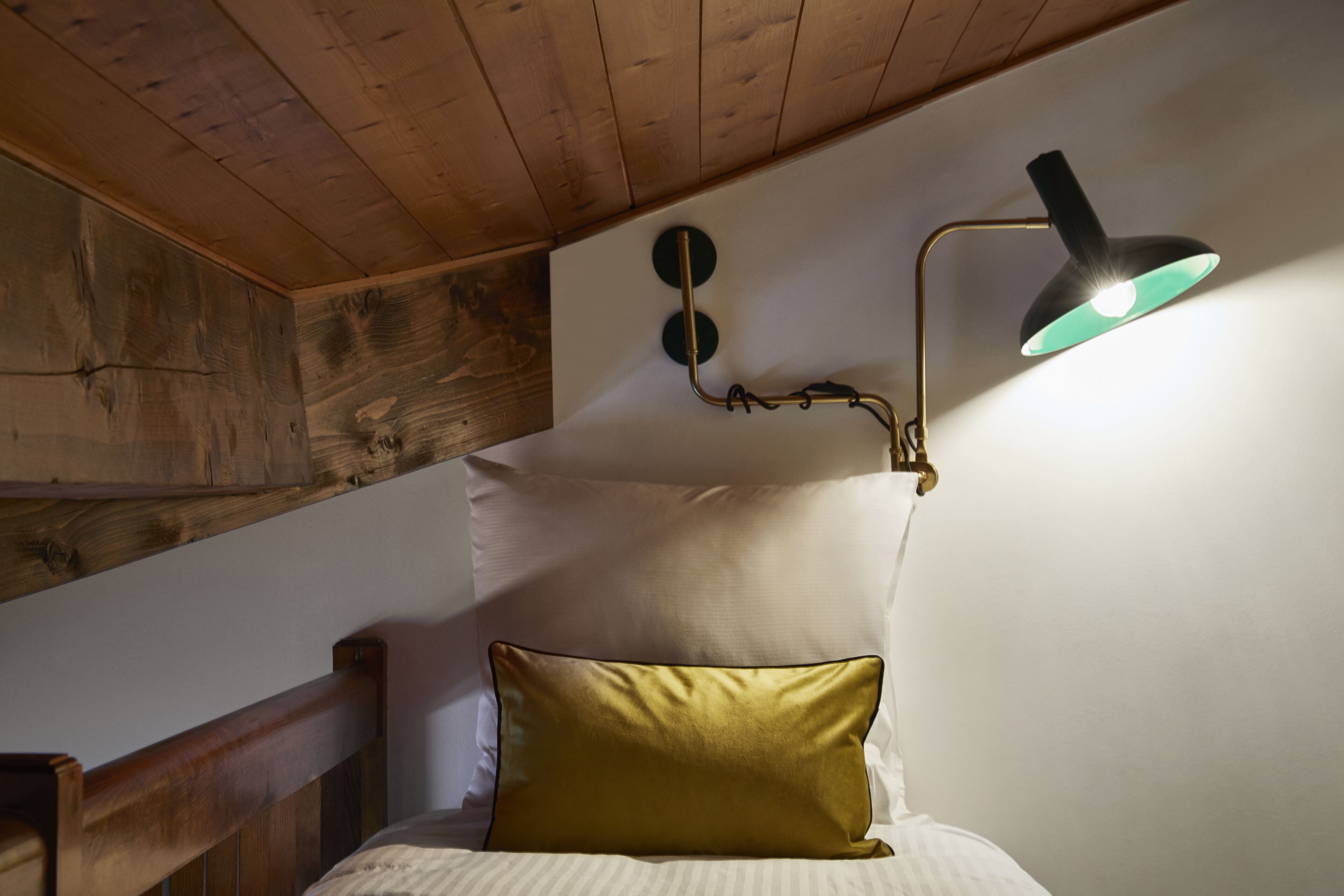 A bedroom with a wooden ceiling, a bed with a gold pillow, and a wall-mounted lamp.