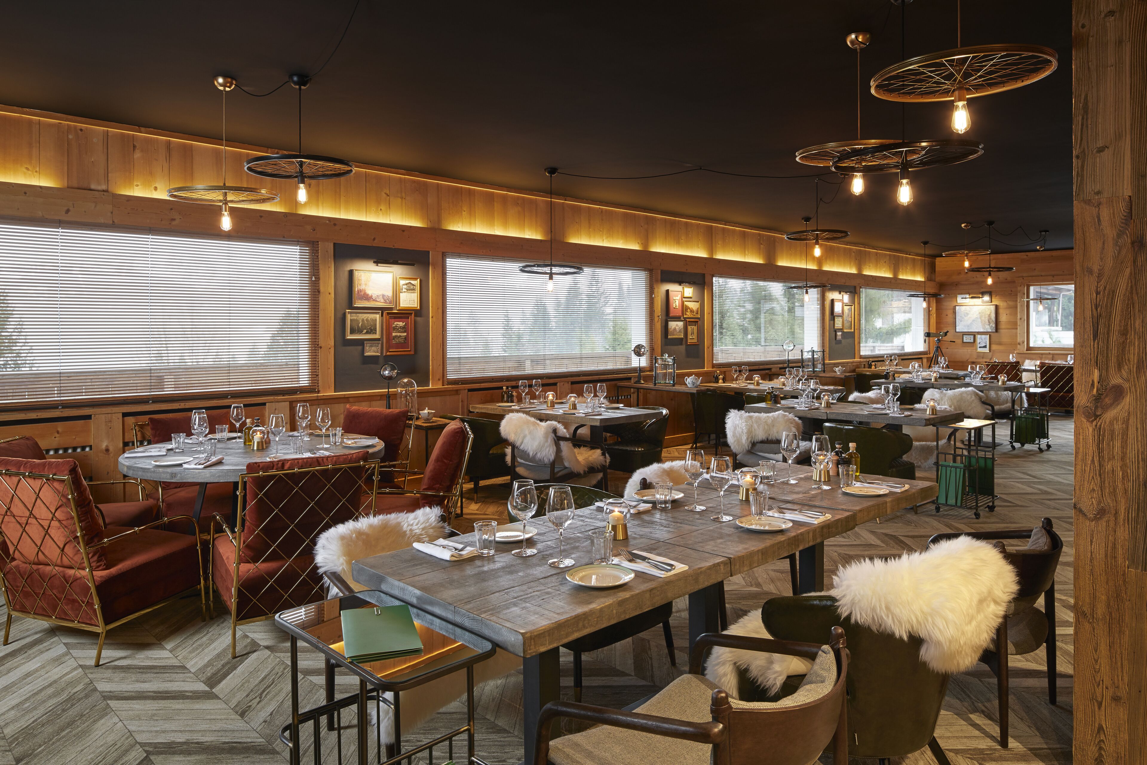 A restaurant with multiple dining tables set for guests, wooden paneling on the walls, and large windows allowing natural light.