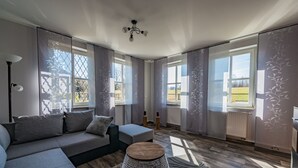 Een moderne woonkamer met een grijze bank, een rond houten bijzettafeltje en een kamerbreed tapijt met een patroon.