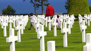 A cemetery with white crosses and a body of water in the background. - La Ferme Manoir Saint Barthélemy (Juaye-Mondaye)