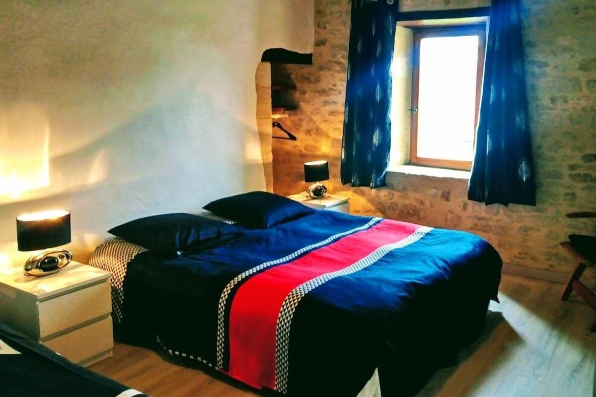 Un dormitorio con cama, lámparas de noche, una ventana con cortinas y techo de madera.