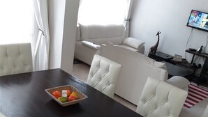 A dining area with a dark wooden table, white upholstered chairs, and a fruit bowl. - Maurica Homes (Nairobi)