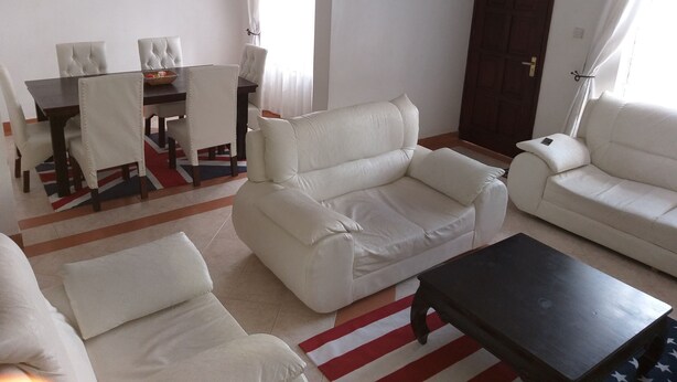 A living room with a sofa, armchairs, a coffee table, and a dining area with chairs and a table. - Maurica Homes (Nairobi)