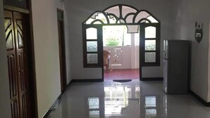 A hallway with a polished floor leading to a room with a large arched doorway. - onelove hostel (Trincomalee)