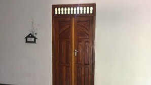 A wooden double door with a traditional design, a small wall-mounted light fixture, and a simple wall decoration. - onelove hostel (Trincomalee)