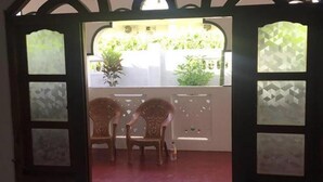 A room with two wicker chairs facing a window with a view of greenery outside. - onelove hostel (Trincomalee)