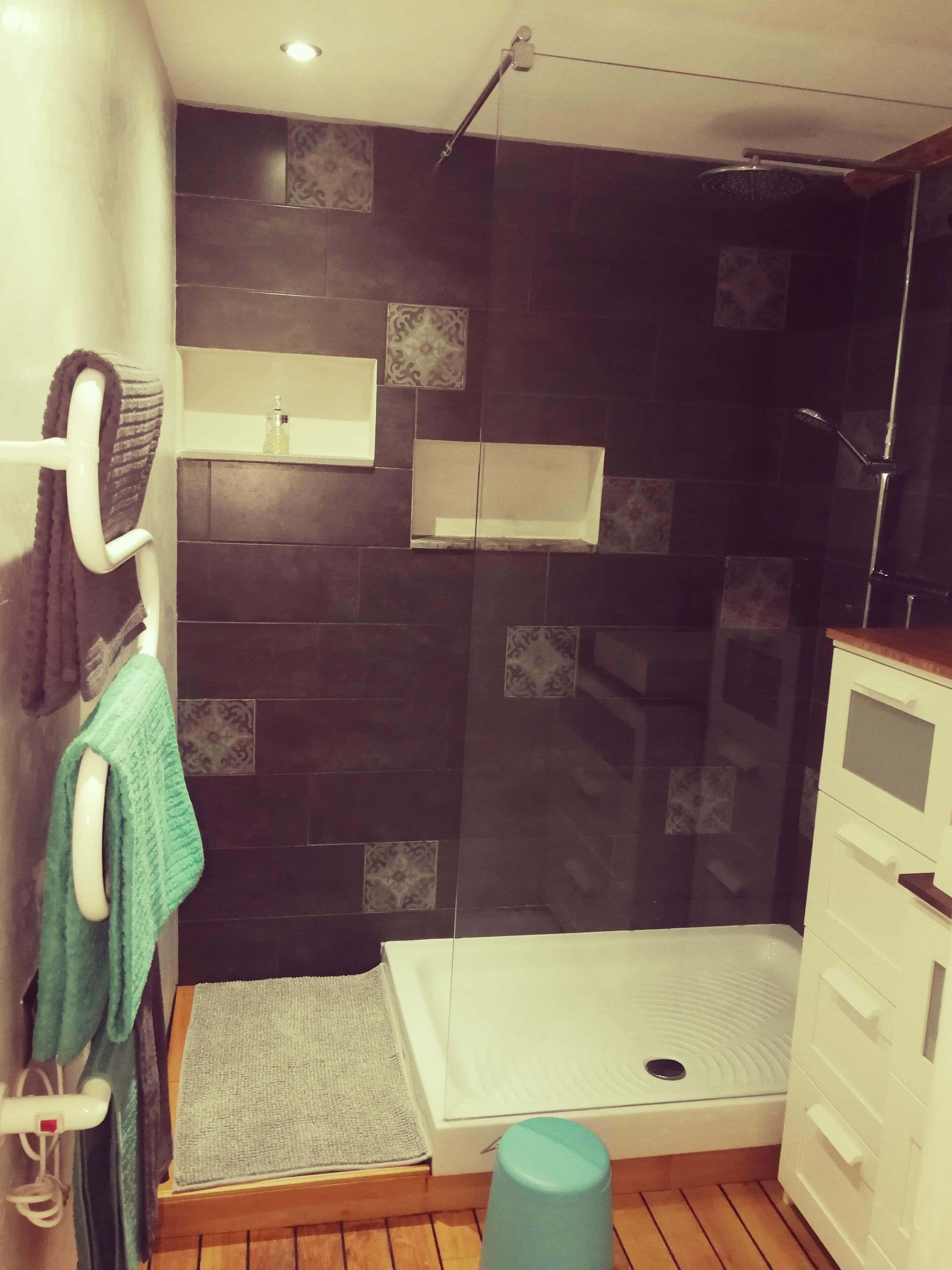 Une salle de bain équipée d’une douche, d’un porte-serviettes, d’un distributeur de savon et d’un petit tabouret.