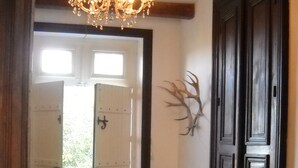 Een gang met een zwart-wit schachbordvloer, een houten stoel, een kroonluchter en een deur met een nummer.