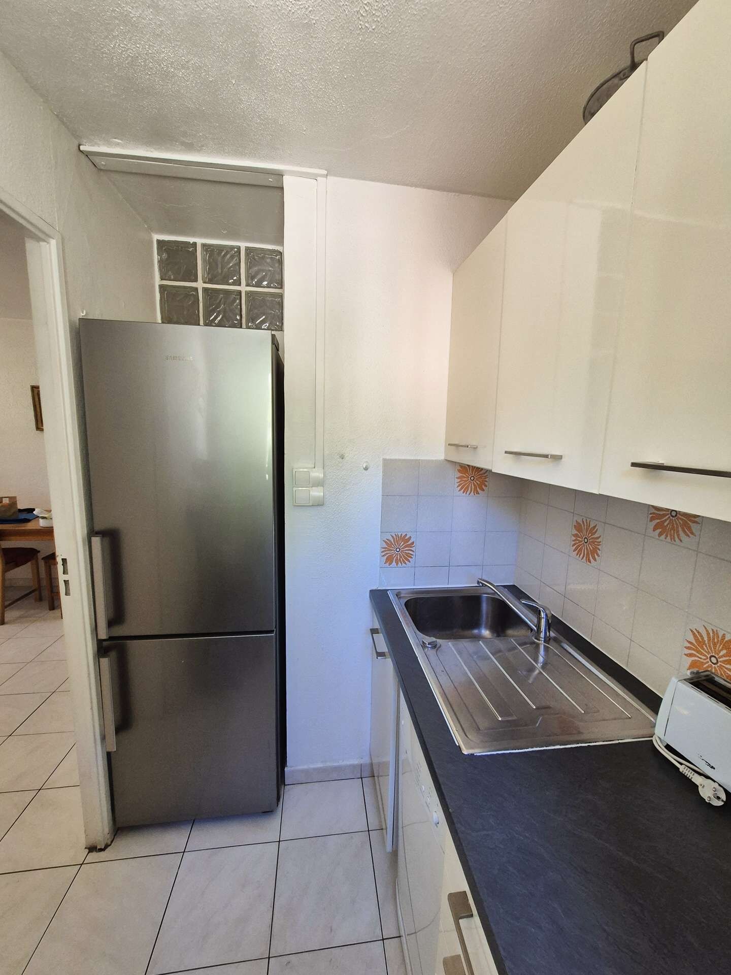 Eine kleine Küche mit einem Edelstahlkühlschrank, einer Spüle und einem Toaster.