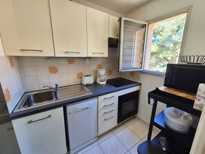 Una cocina compacta con gabinetes blancos, cafetera, tostadora y lavavajillas.