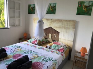 Ein Schlafzimmer mit einem Bett, einem Nachttisch, einer Lampe, einem Fenster und einer Wand mit einer Wanddekoration.