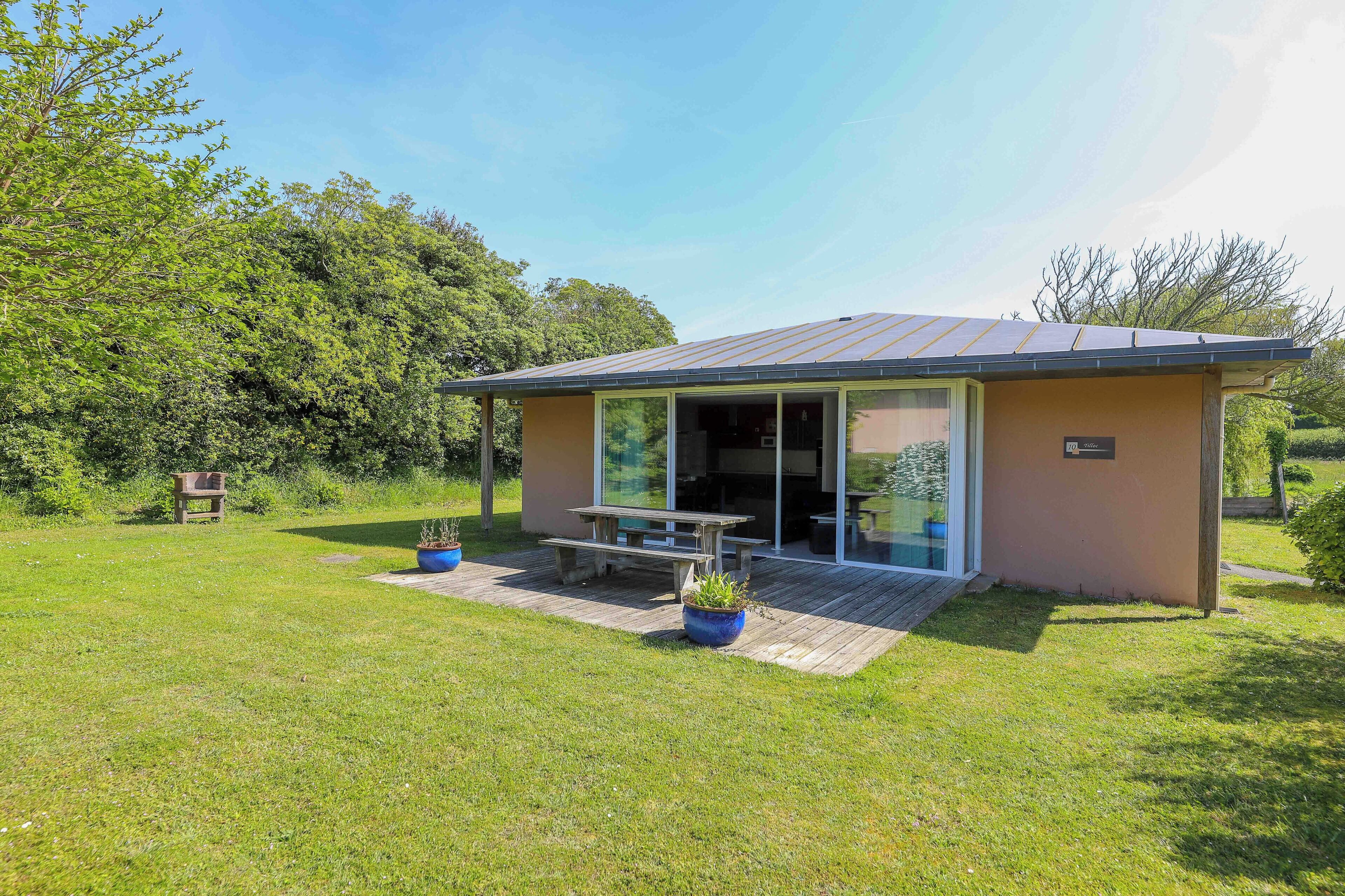 A small, single-story building with a patio area, a wooden deck, and a glass door entrance.