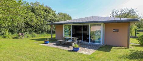 A small, single-story building with a patio area, a wooden deck, and a glass door entrance.