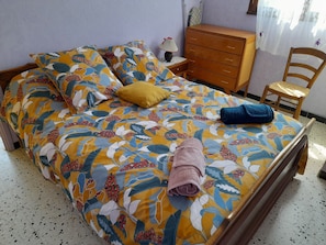 Un lit avec une couvre-lit à motifs floraux, une commode en bois, une chaise et une table de chevet avec une lampe.