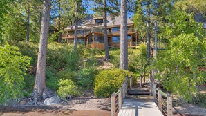 A wooden cabin with a deck leading to a glass balcony, surrounded by dense forest. - Anchors Aweigh - Lakefront - TLUXP (Tahoe City)