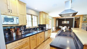 A modern kitchen with wooden cabinets, a black countertop, a built-in microwave, and a large island with a stove. - Black Bear Ranch -Large home near Bozeman's Hyalite Canyon with peace & quiet (Bozeman)