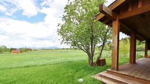 A wooden cabin with a porch overlooking a grassy field and a tree. - Black Bear Ranch -Large home near Bozeman's Hyalite Canyon with peace & quiet (Bozeman)