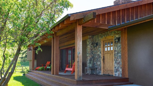 A wooden porch with a stone wall and a wooden door. There are three red chairs on the porch. - Black Bear Ranch -Large home near Bozeman's Hyalite Canyon with peace & quiet (Bozeman)