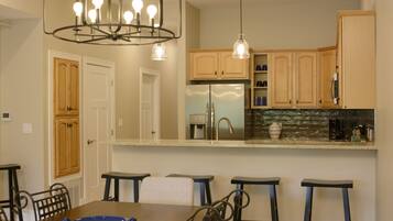 A modern kitchen with wooden cabinets, a stainless steel refrigerator, and a bar area with stools.