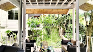 Een balkon buiten met rieten meubilair, een fruitmand en uitzicht op weelderige begroeiing.