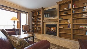 Una sala acogedora con chimenea, estanterías, televisor y mobiliario de cuero.