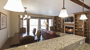 Un comedor con una mesa y sillas de madera, una chimenea y un televisor montado en la pared.