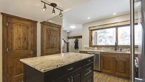 Una cocina con armarios de madera, encimeras de granito, un refrigerador de acero inoxidable y una ventana con vista a árboles.