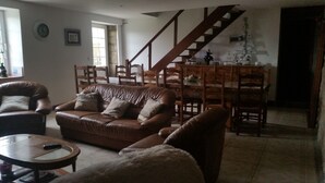 Un salon avec un canapé en cuir marron, une table basse ronde et un fauteuil moelleux blanc. Un escalier mène à une salle à manger avec des chaises et une table en bois.