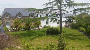 Un bâtiment en pierre doté de nombreuses fenêtres en lucarne et d’un jardin bien entretenu, agrémenté de diverses plantes et d’une pelouse.