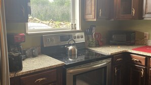 Una cocina con estufa, horno, microondas y una ventana con cortinas.