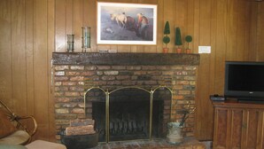 A fireplace with a brick surround, a framed painting above it, and a television on a wooden cabinet to the right.