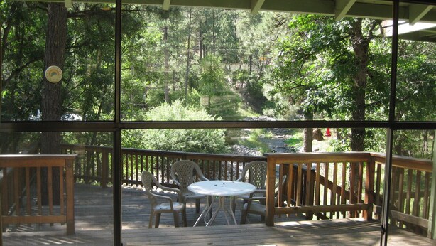 A wooden deck with a table and chairs, surrounded by a wooden railing, overlooking a forested area.