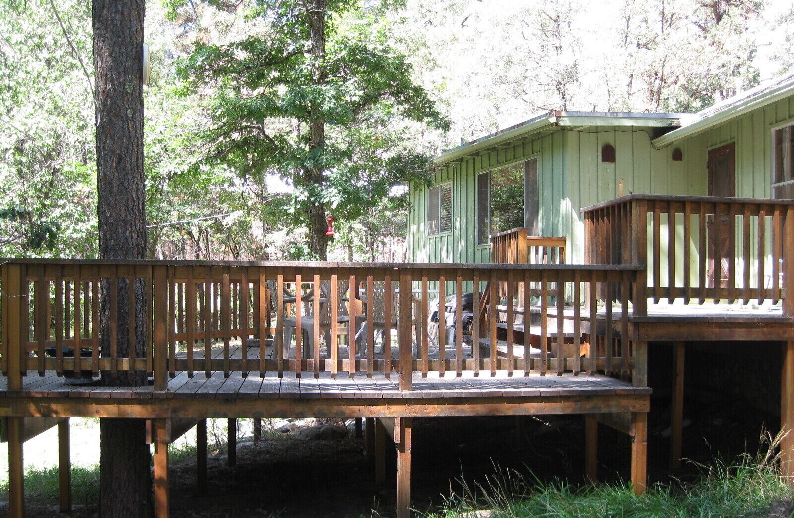 Une terrasse en bois avec un banc, entourée d’arbres et d’un petit bâtiment doté d’un porche.