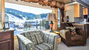 Een gezellige woonkamer met uitzicht op een besneeuwde stad, een gestreept bankje, een leren fauteuil en een lamp.