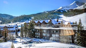 Een besneeuwde lodge met meerdere gebouwen, een skipiste en een berg op de achtergrond.