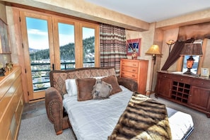 Un dormitorio con una cama grande, cómoda de madera y vista a un paisaje nevado por la ventana.
