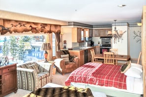 Habitación de hotel con cama, sofá, sillón, una mesita, escritorio, kitchenette y un ventanal con vistas a edificios.