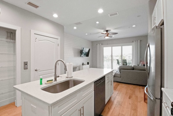 A modern kitchen with a built-in dishwasher, a large island with a sink, and a ceiling fan.