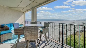 Un balcón con muebles de mimbre, vista a la playa y cielo despejado.
