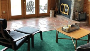 Een blokhut interieur met een stenen open haard, houten vloeren en een groen vloerkleed.