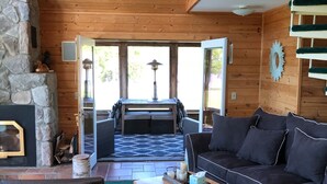 Een gezellig blokhutinterieur met een stenen openhaard, houten plafond en een comfortabele zithoek met een bank en fauteuils.