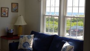Un salon avec un canapé bleu, une lampe et une fenêtre donnant sur la mer et les voitures garées.