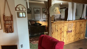 Ein gemütliches Wohnzimmer mit einem roten Sessel, Holzvertäfelung, einer Vintage-Uhr und rustikalen Einrichtungsgegenständen.