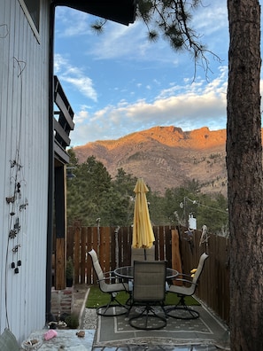 Un patio con una mesa y sillas, un paraguas amarillo y vistas a las montañas.