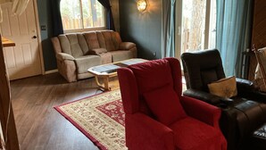 Ein Wohnzimmer mit einer Couch, einem roten Sessel, einem Couchtisch und einem Ventilator.
